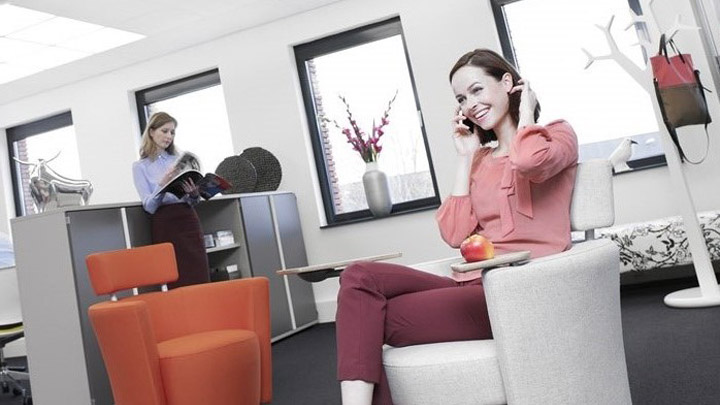 سيدة تتحدث في الهاتف وتقف أسفل وحدة Soundlight Comfort. إضاءة مثالية للمكاتب لتأسيس أماكن عمل أكثر راحة.